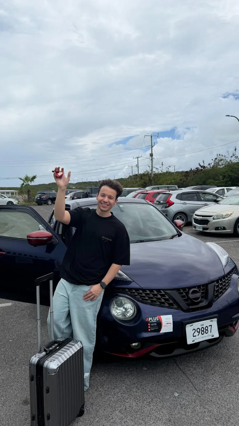 Traveler smiling beside his rental car with the key